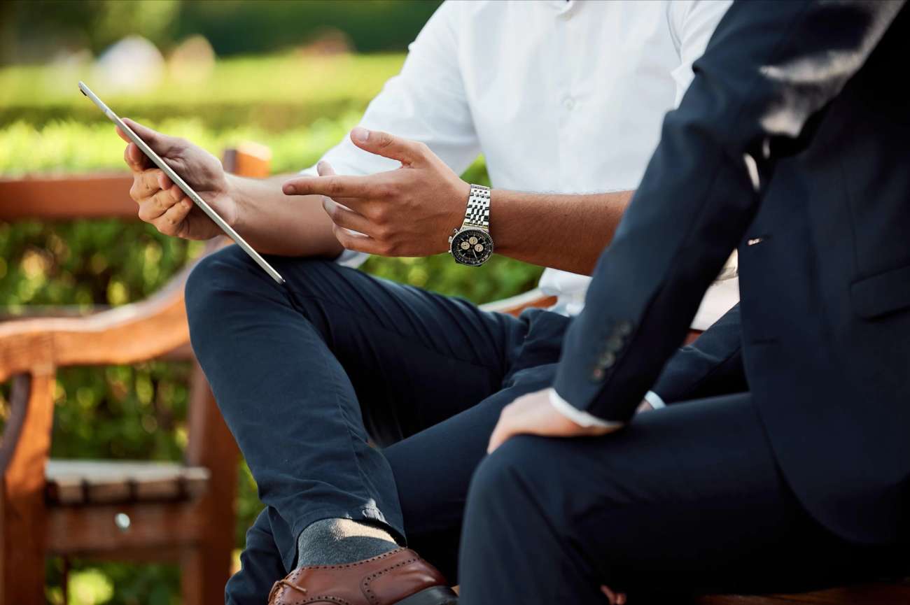 Two people in suits sitting on bench pointing at tablet