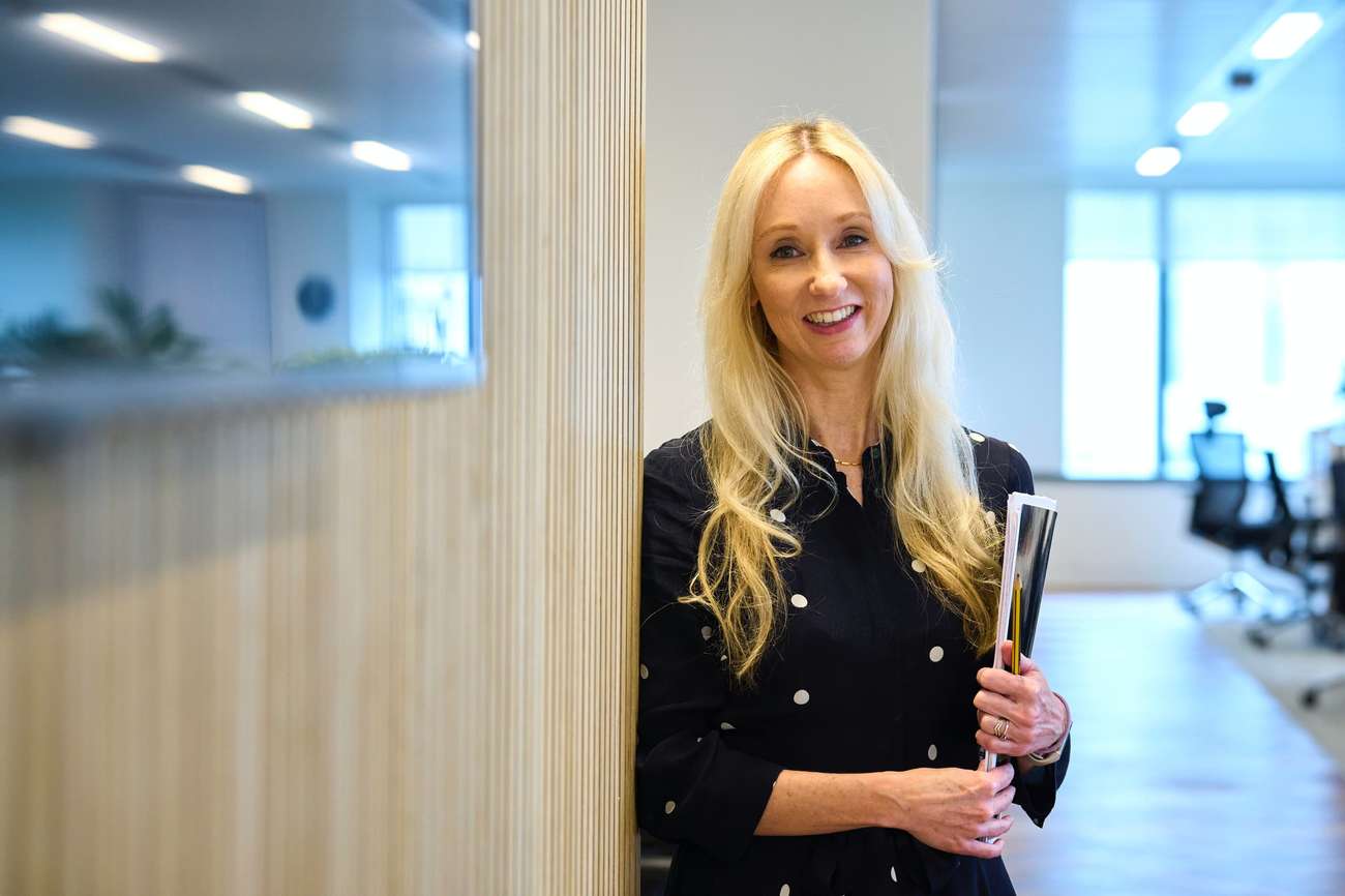 Person in office leaning against wall smiling in camera